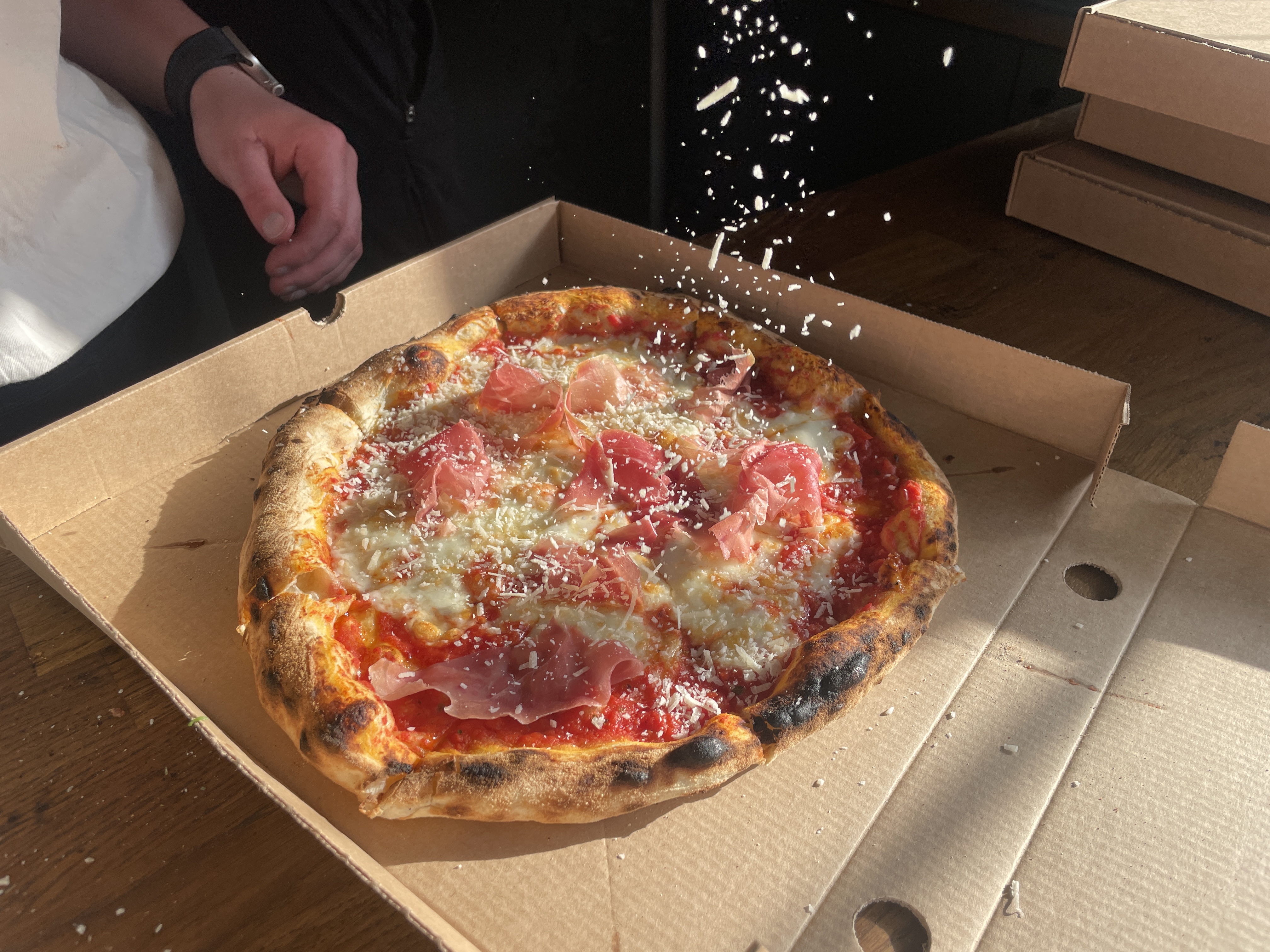Nybakad pizza i kartong toppas med riven ost